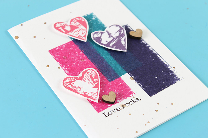 Adhere heart images to card panel with dimensional adhesive and add embellishments as needed in step 4 of a Valentine's Day card tutorial